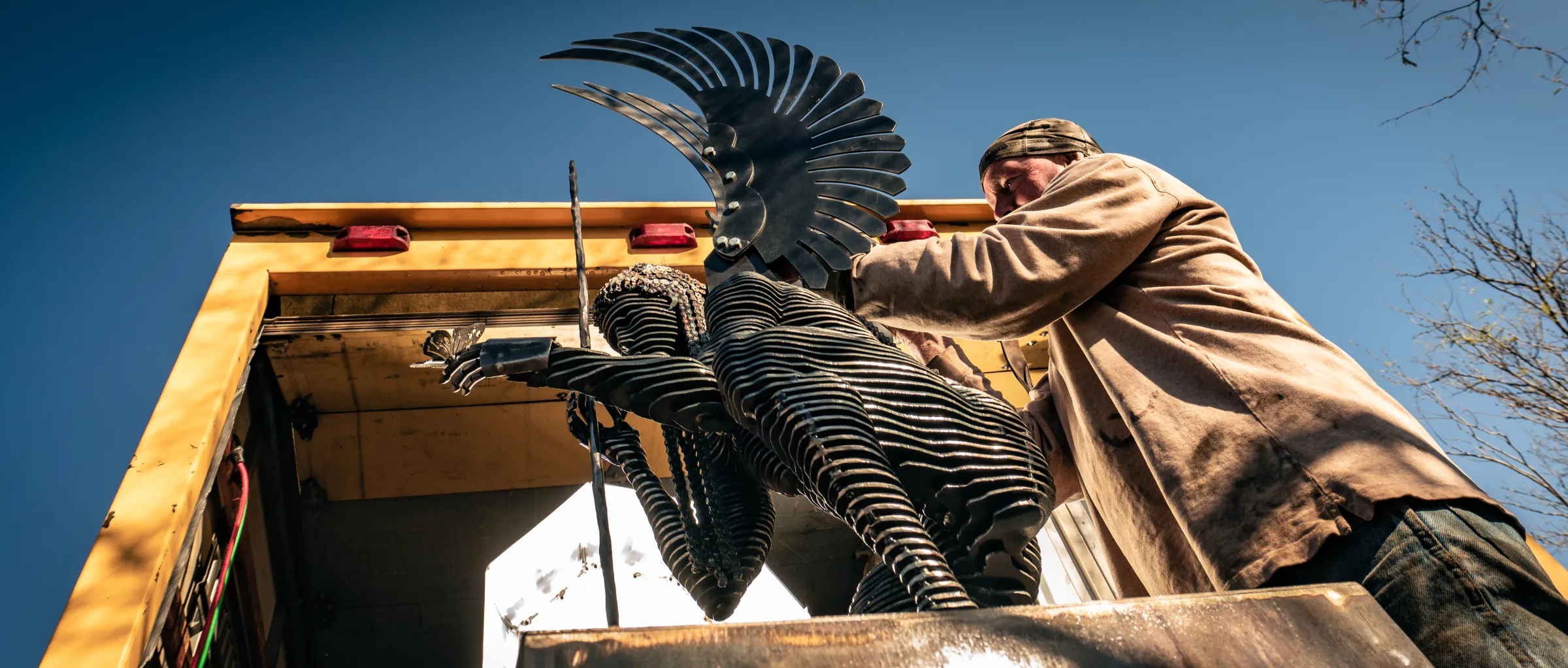 John beside a large winged sculpture on a flatbed, on its way to install